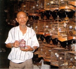 Vendeur d'oiseau en cage, buvant son thé dans une tasse à couvercle traditionnelle.